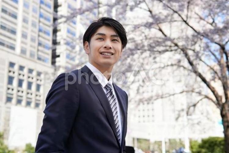桜を背景に笑顔で立つビジネスマン	 ビジネスマン,男性,新入社員の写真素材