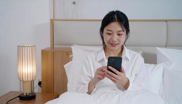 ベッドルームでスマホを見る日本人女性 ベッドルームでスマホを見る日本人女性の写真