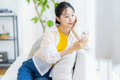 部屋でスマホを操作する女性 部屋でスマホを操作する女性 スマホ,笑顔,部屋の写真素材