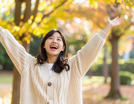 秋の公園で両手を広げて笑顔を見せる女性の写真