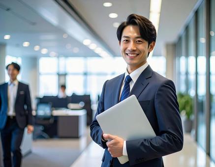 オフィスでPCを持って微笑む社員 オフィスでPCを持って微笑む社員の写真