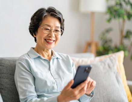 自宅のリビングでスマホを操作する女性 自宅のリビングでスマホを操作する女性の写真
