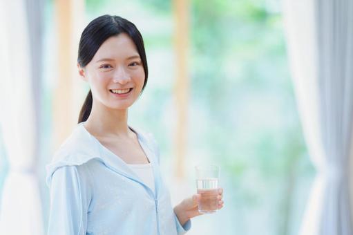 水のコップを持ち笑う黒髪の女性の写真