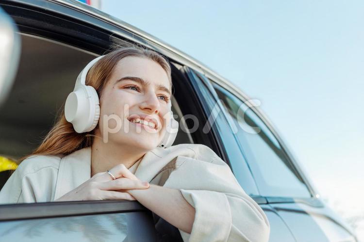 車から腕と顔を出して音楽を聴く女性（笑顔） 女性,窓,顔出すの写真素材