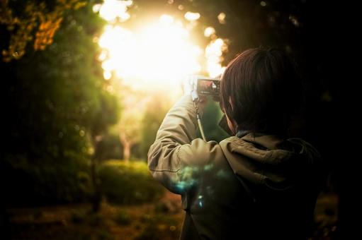 ＜素材＞夕暮れの森で夕日を撮影する女性 女性,サンセット,夕方の写真素材