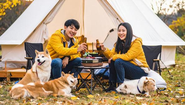 秋冬のキャンプ場で乾杯する犬連れの男女 秋冬のキャンプ場で乾杯する犬連れの男女の写真