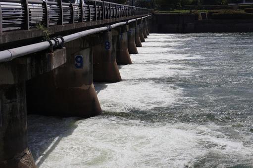 洗堰から放水される水と川の写真