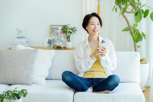 部屋でスマホを使うミドル女性 スマホ,笑顔,女性の写真素材