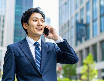 街中で電話をかける若い男性社員 街中で電話をかける若い男性社員の写真