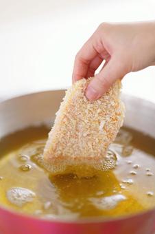 油鍋にとんかつを入れる手の写真