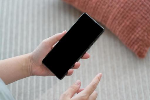 リビングでスマホを持っている女性の手元 リビングでスマホを持っている女性の手元 スマホ,部屋,手の写真素材