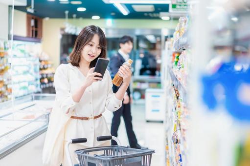スーパーの商品をスマホで調べる若い女性 スーパーの商品をスマホで調べる若い女性 調べる,アプリ,女性の写真素材