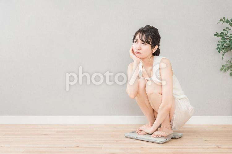 体重計に乗って考えるスリムなアジア人女性 体重,考える,ダイエットの写真素材