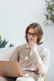 顎を触りながら膝の上のノートパソコンを使う長髪男性 男性,外国人,欧米人の写真素材