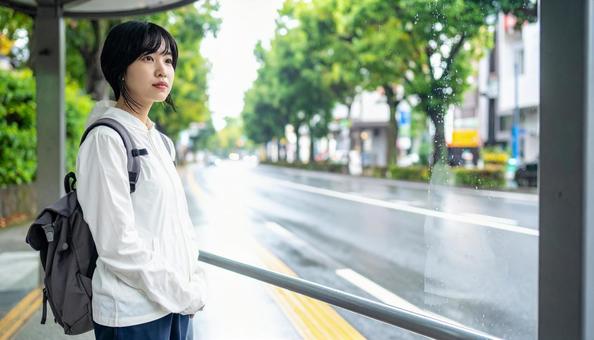 雨の中バス停でバスを待つ日本人女性の写真