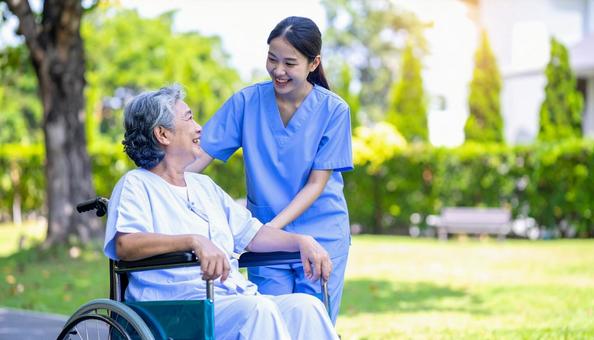 散歩する車椅子の高齢女性と女性介護士 散歩する車椅子の高齢女性と女性介護士の写真