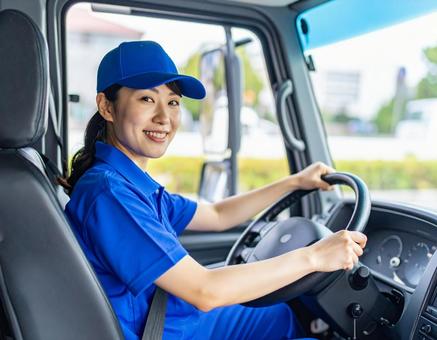 笑顔でトラックを運転する女性ドライバー 笑顔でトラックを運転する女性ドライバーの写真