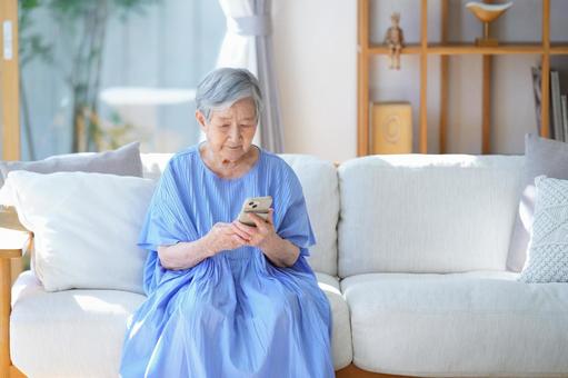 ソファでスマホを見ている女性 女性,スマートフォン,持つの写真素材