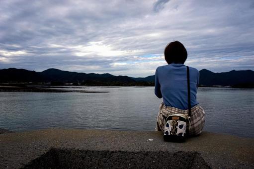 ＜素材＞防波堤の先きに座り海を見る女性 女性,海,鬼岳の写真素材