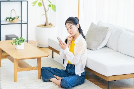 部屋でスマホを操作する女性 部屋でスマホを操作する女性 スマホ,笑顔,部屋の写真素材