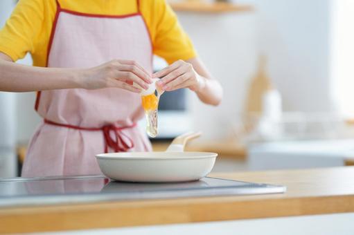 フライパンに卵を割り落とす手元の写真