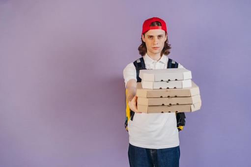 ピザ箱を重ねて持っているフードデリバリーの男性（紫背景） 配達,フードデリバリー,デリバリーの写真素材