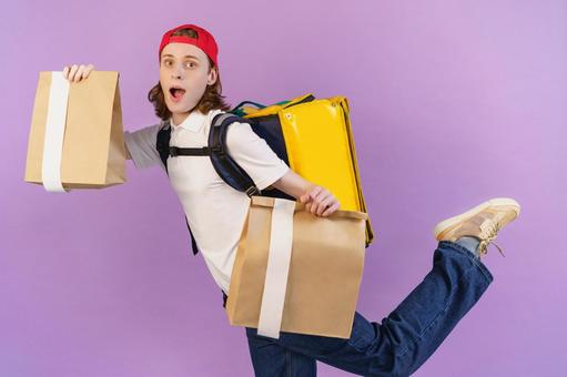 紙袋を持つ片足を上げたフードデリバリーの男性 配達,フードデリバリー,デリバリーの写真素材