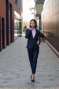 街なかを電話しながら歩いているパンツスーツの女性 ビジネスウーマン,ビジネス,女性の写真素材