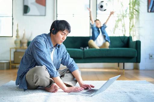 絨毯に座ってパソコンをする男性と後ろでサッカーボールで遊ぶ男の子 絨毯に座ってパソコンをする男性と後ろでサッカーボールで遊ぶ男の子 親子,男の子,小学生の写真素材
