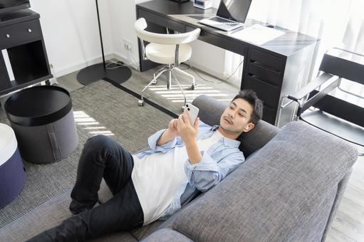 ソファーでスマートフォンを使う男性 ソファーでスマートフォンを使う男性 男性,人物,スマートフォンの写真素材