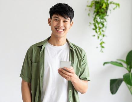 室内でスマートフォンを持つ笑顔の男性 室内でスマートフォンを持つ笑顔の男性の写真