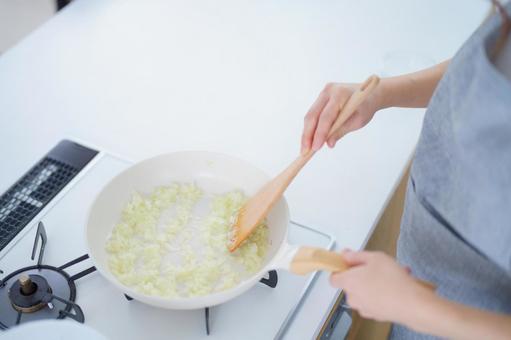フライパンを持ち玉ネギのみじん切りを炒める人の手 フライパンを持ち玉ネギのみじん切りを炒める人の手の写真
