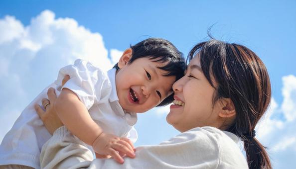 青空の下、子供を抱っこする母親 青空の下、子供を抱っこする母親の写真