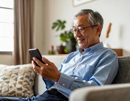 自宅のリビングでスマホを操作する男性 自宅のリビングでスマホを操作する男性の写真