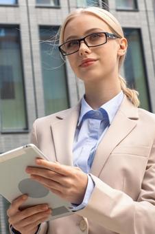 オフィスビルの外でタブレットを持って立っているメガネを掛けた外国人女性 ビジネスウーマン,ビジネス,女性の写真素材