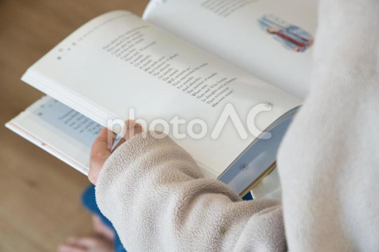 自宅で腰掛けて英文の本を読んでいる女性 本,読書,手元の写真素材