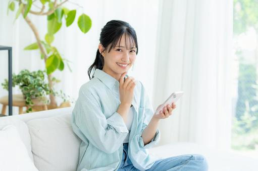 部屋でスマホを操作する若い女性 スマホ,笑顔,女性の写真素材