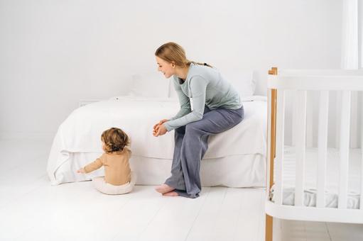 ベッドに座り笑顔で子供を見つめる母 ベッドに座り笑顔で子供を見つめる母 親子,母子,赤ちゃんの写真素材