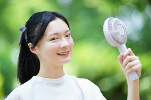 白いノースリーブの女性が笑顔でハンディファンを見つめるの写真