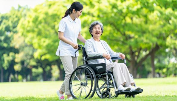 車椅子を押してシニア女性と笑う若い介護士 車椅子を押してシニア女性と笑う若い介護士の写真