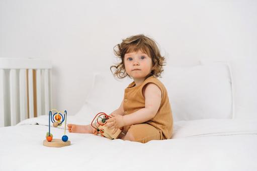 玩具を持ちベッドでお座りする子 玩具を持ちベッドでお座りする子 赤ちゃん,かわいい,玩具の写真素材