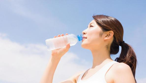 水分補給をするタンクトップの女性 水分補給をするタンクトップの女性の写真