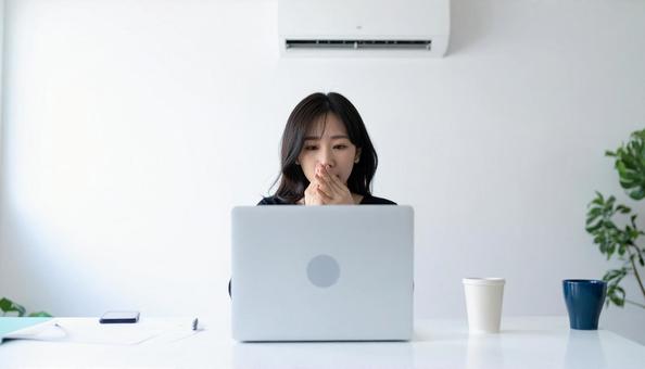 部屋のエアコンの下で寒がる女性 部屋のエアコンの下で寒がる女性の写真