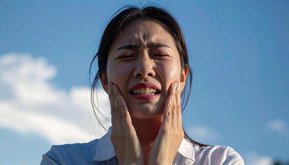 歯が痛んで手で押さえる女性の写真