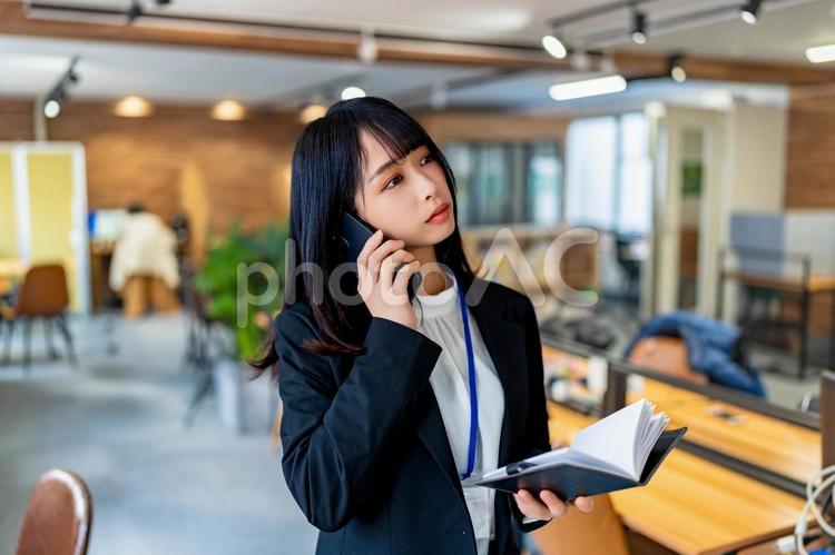 手帳を開きながら電話をするスーツ姿の女性 女性,ビジネス,ビジネスウーマンの写真素材