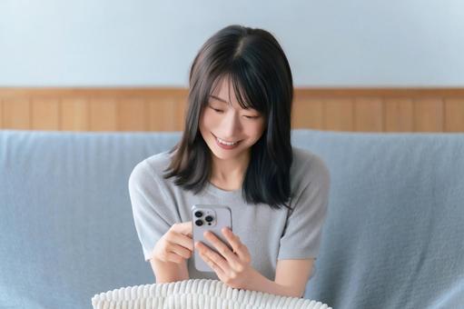 ソファに座ってスマホを使う笑顔の女性 ソファに座ってスマホを使う笑顔の女性の写真