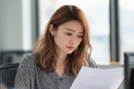 資料を見て悩むビジネス女性の写真