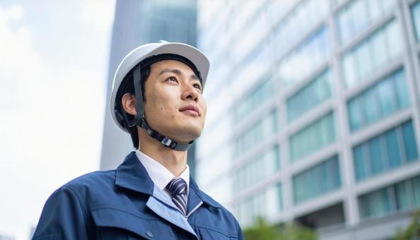 高層ビルの斜め上を見つめる若い作業服男性 高層ビルの斜め上を見つめる若い作業服男性の写真