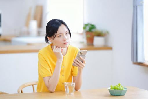 スマホを持ち考える黄色い服の女性の写真