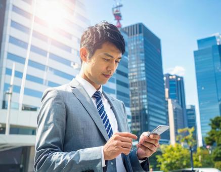 オフィス街でスマホを操作する男性社員の写真
